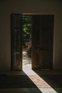 A rustic wooden door opens to reveal a sunlit garden, creating a serene and welcoming atmosphere.